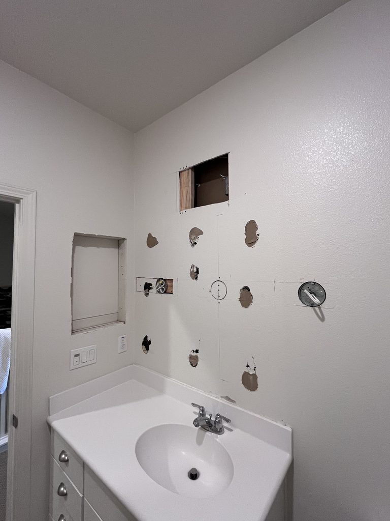 Bathroom vanity wall with a dozen open holes and cut-outs left from plumbing and fixture work, before drywall repair