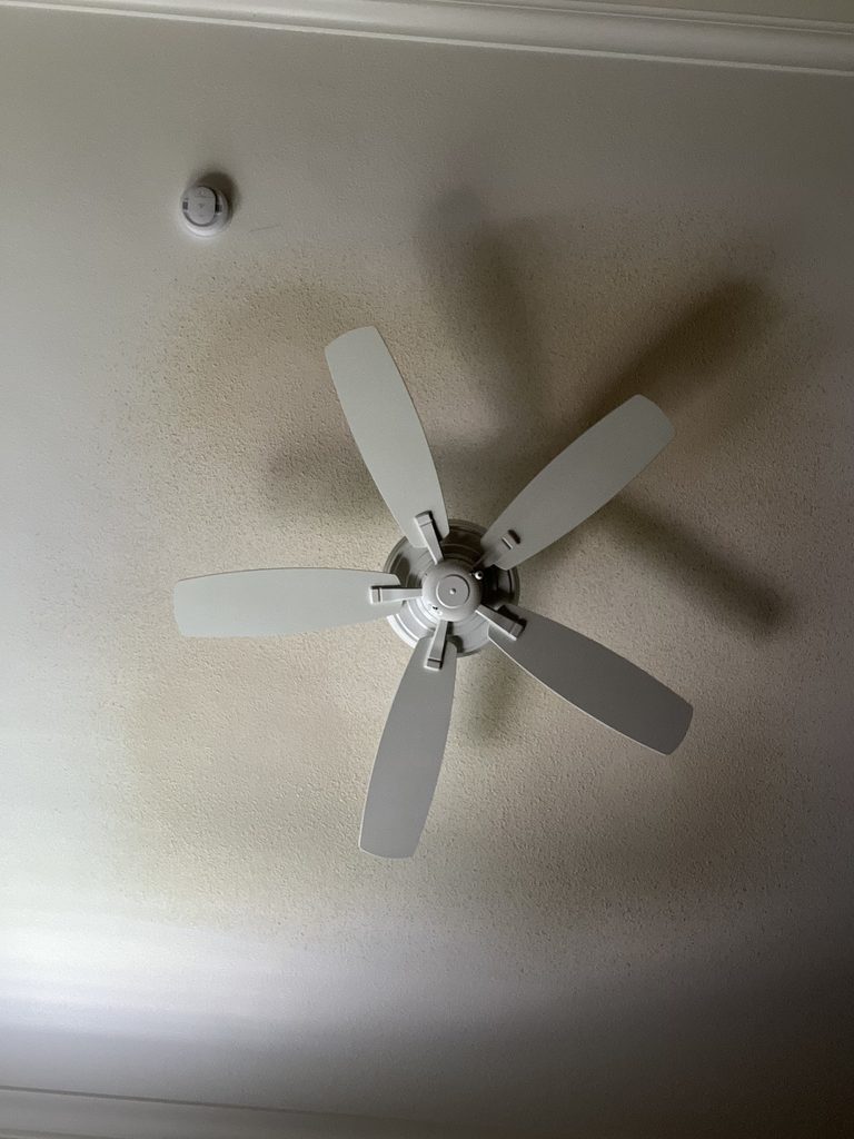 Textured ceiling around a ceiling fan showing brown water staining before repair