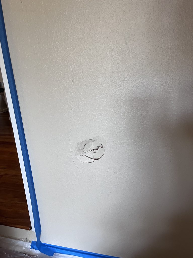 Drywall patch with joint compound applied and blue painter's tape masking the trim